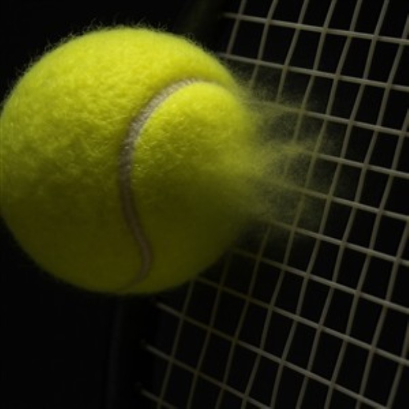 Energi fra Tennisboldens Slag - Oplev intensiteten i spillet med dette nærbillede af en tennisbold, der rammer nettet med kraft. De flyvende støvpartikler tilføjer en dynamisk og energisk stemning til dit rum.